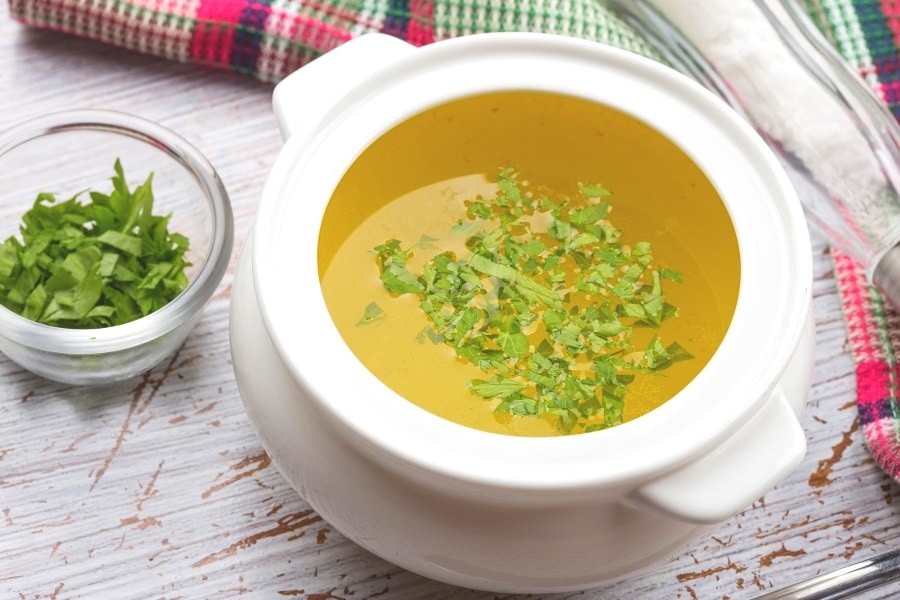 A bowl of bone broth with garnishes next to it for getting rid of stomach bloat quickly