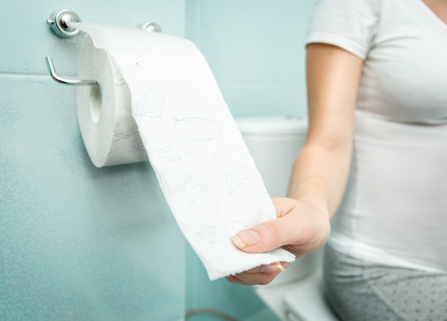 A women sitting on a toilet reaching for toilet paper against a blue wall