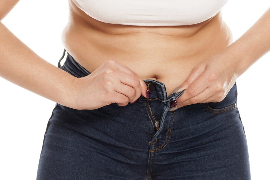 A woman struggling to button her pants