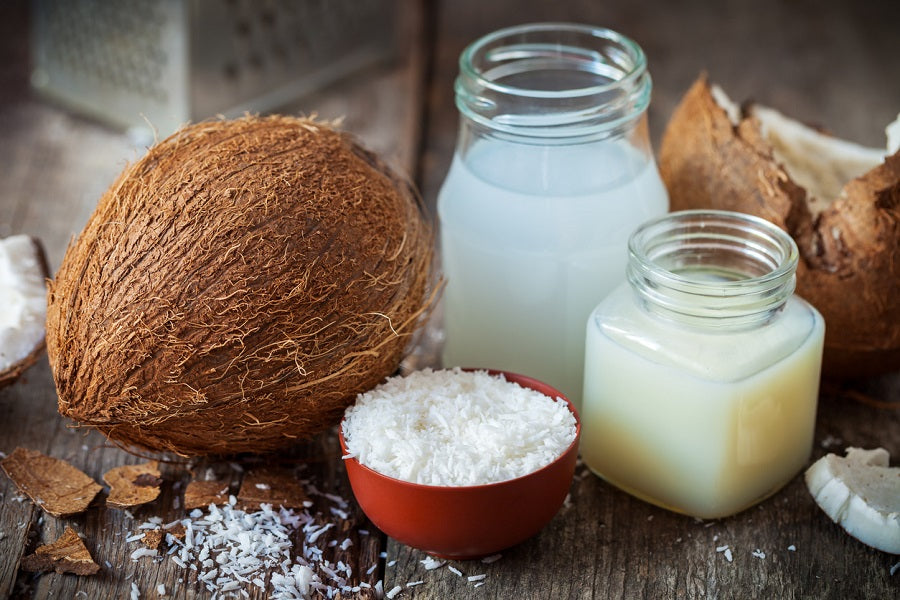 A coconut next to glass jars of milk and shaved coconut