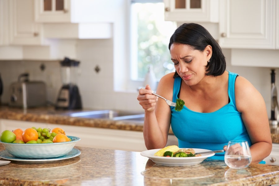 A woman sitting in her kitchen eating broccoli