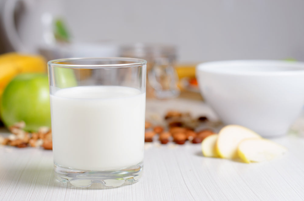 glass of a healthy milk alternative with fruits and nuts in background