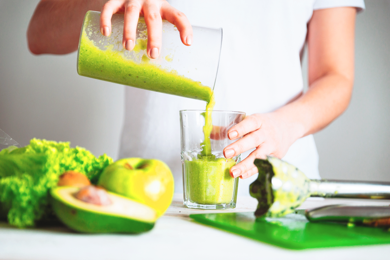 woman pouring green smoothie into glass
