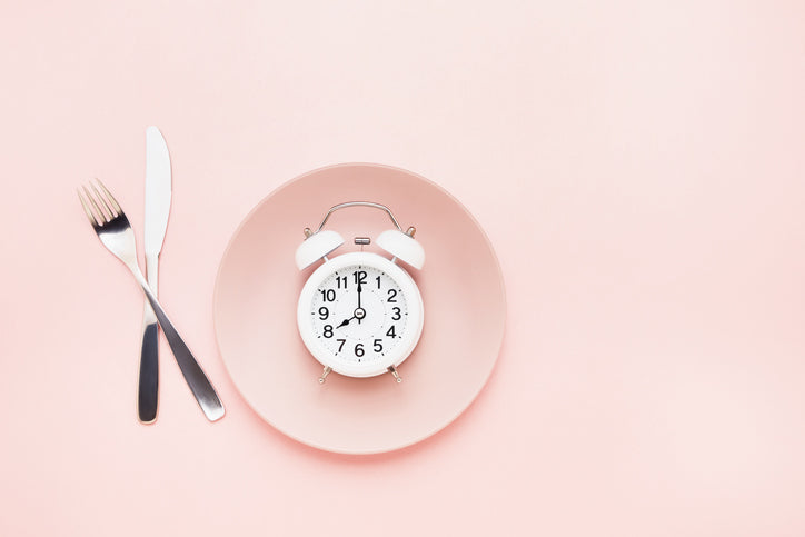 A pink plate with a clock on it with a fork and knife to the left