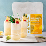 Three glasses of a tropical drink with pineapple and cherries, next to a box of Dr. Kellyann Collagen Cooler on a light blue background.
