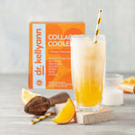 Orange-colored drink in a glass with a straw, next to a box of Dr. Kellyann Collagen Coolers on a light background.